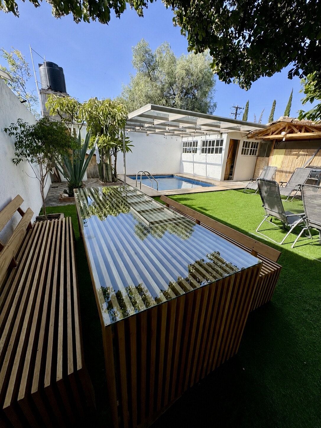 Mesa de jardín con cubierta de cristal y bancas de madera maciza de roble americano junto a una alberca